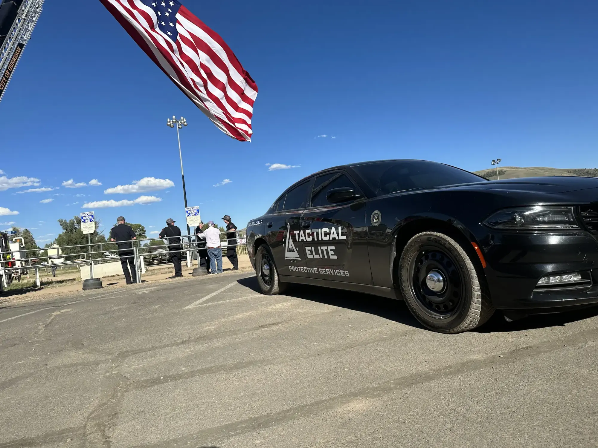 Tactical Elite Protective Services patrol vehicle parked beneath an American flag at an event site