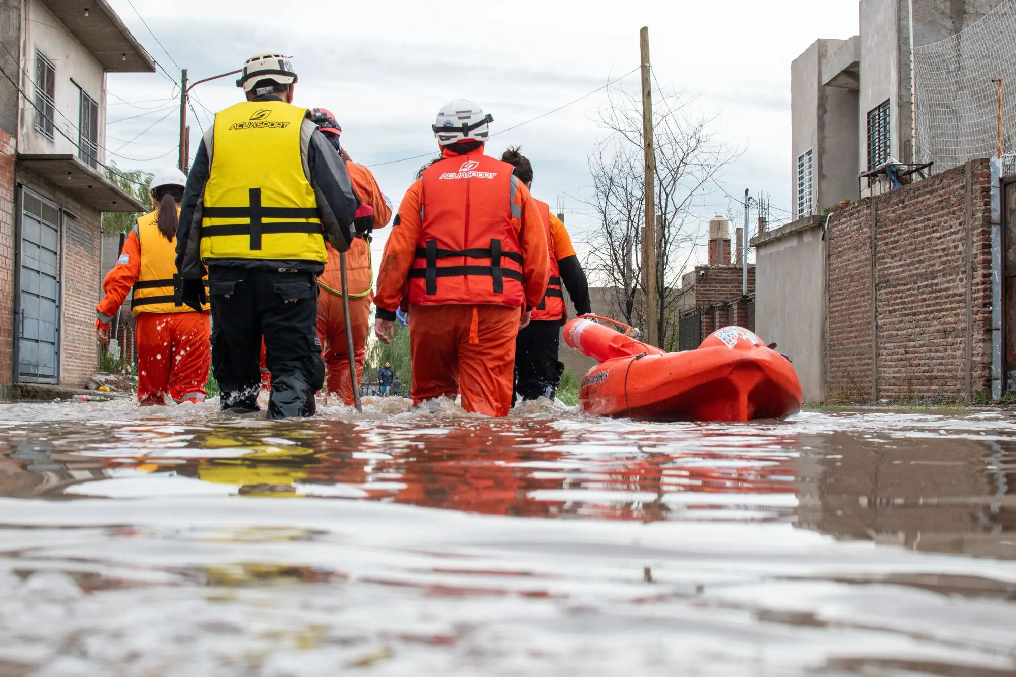 Rescue team in life vests and helmets wading through a flooded street towing a raft