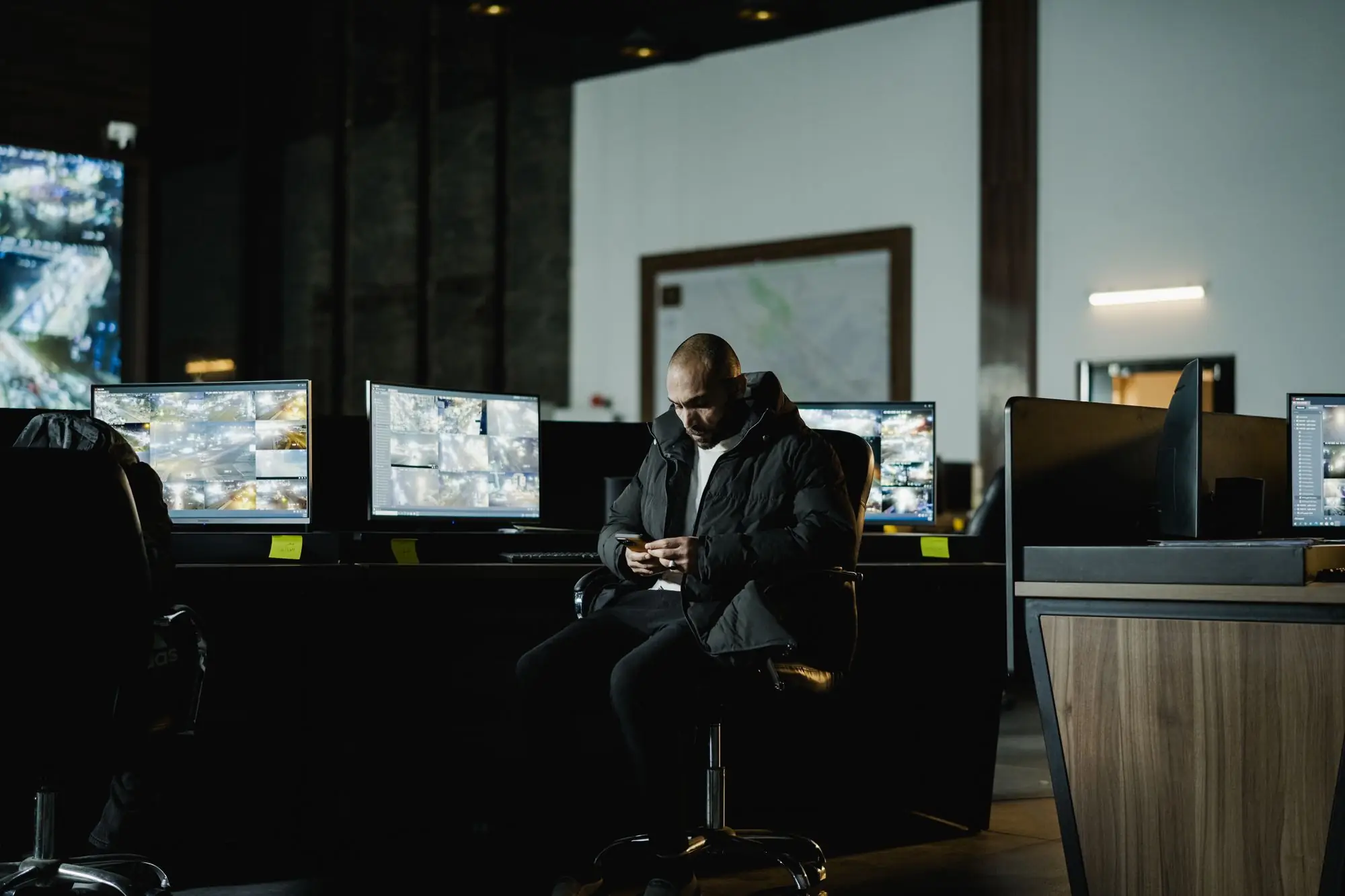Investigator reviewing footage in a dark monitoring room lined with CCTV screens