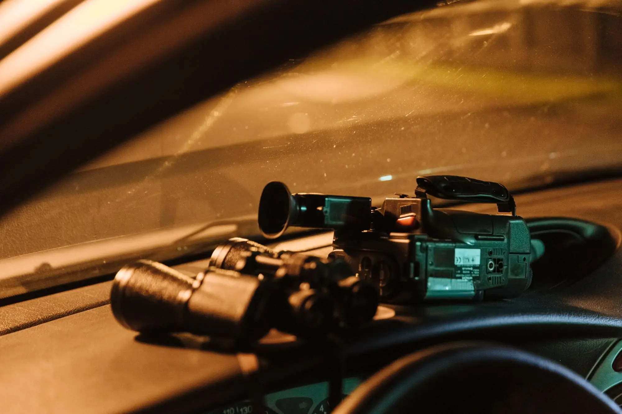 Camcorder and binoculars on a car dashboard during a night surveillance operation