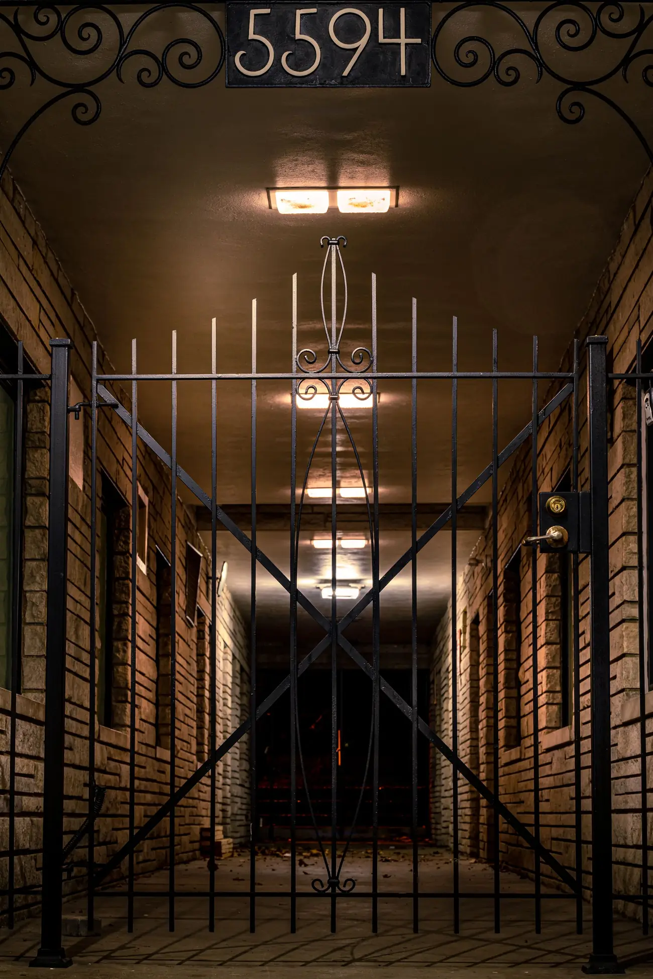 Locked security gate closing off a lit apartment breezeway at night