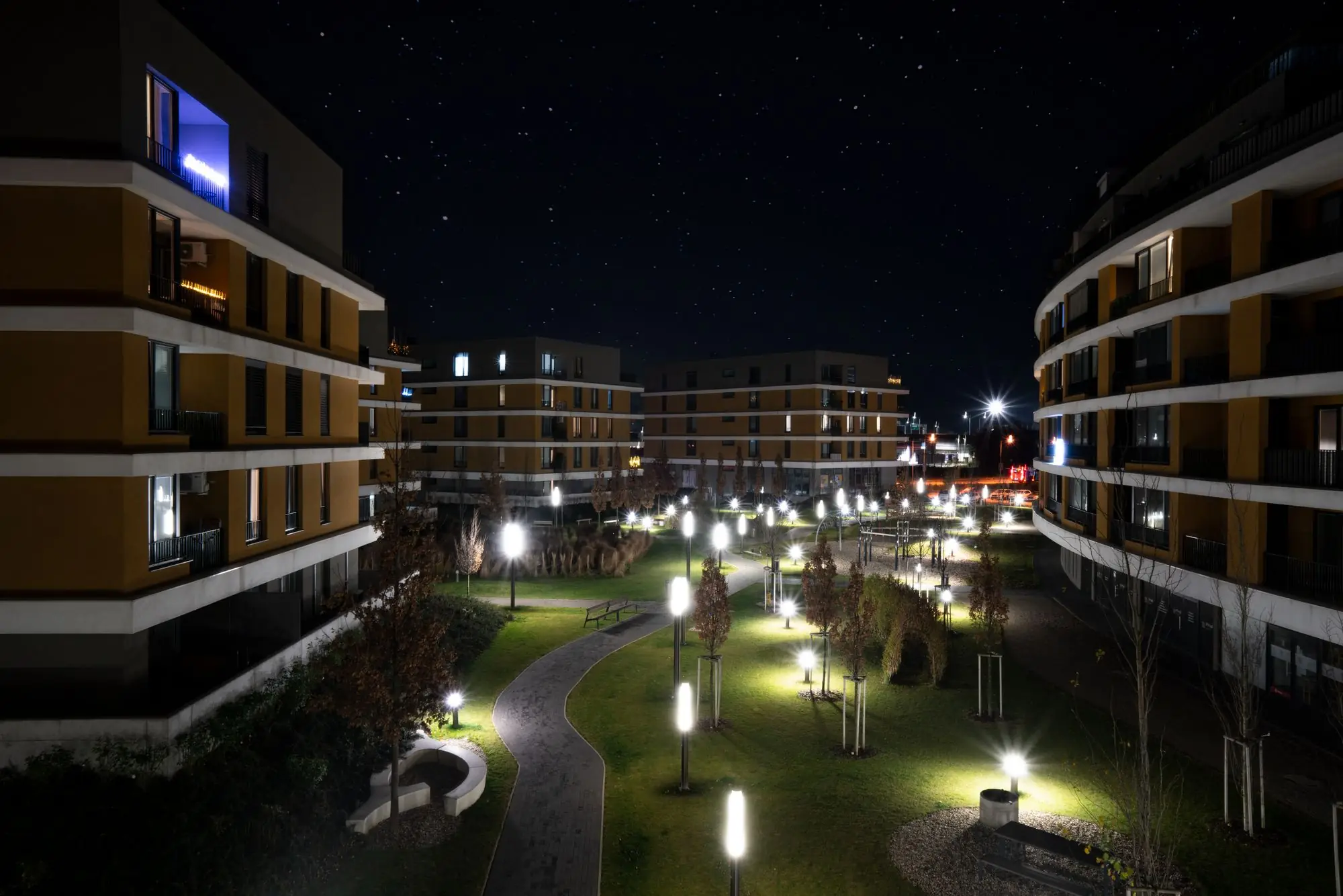 Apartment community courtyard at night, lit paths running between buildings with balconies